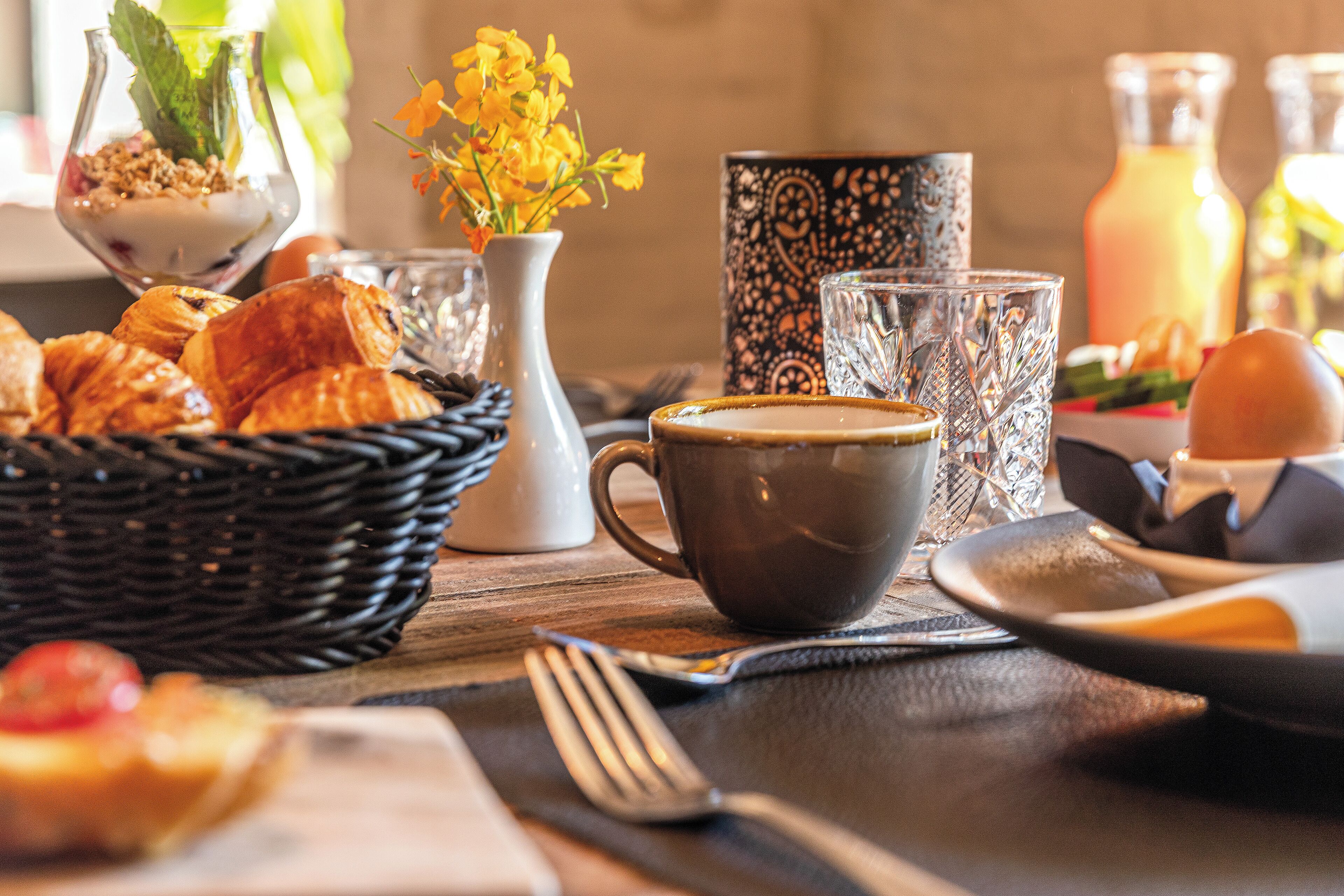 Une table mise pour le petit-déjeuner avec des croissants, une tasse de café et un vase rempli de fleurs jaunes.