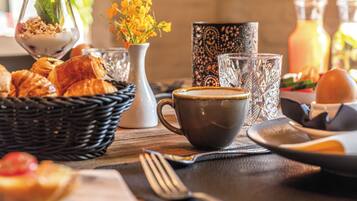 Une table mise pour le petit-déjeuner avec des croissants, une tasse de café et un vase rempli de fleurs jaunes.