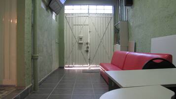 Un pasillo estrecho con un sofá rojo, una mesa blanca y una puerta cerrada con un ventanal.