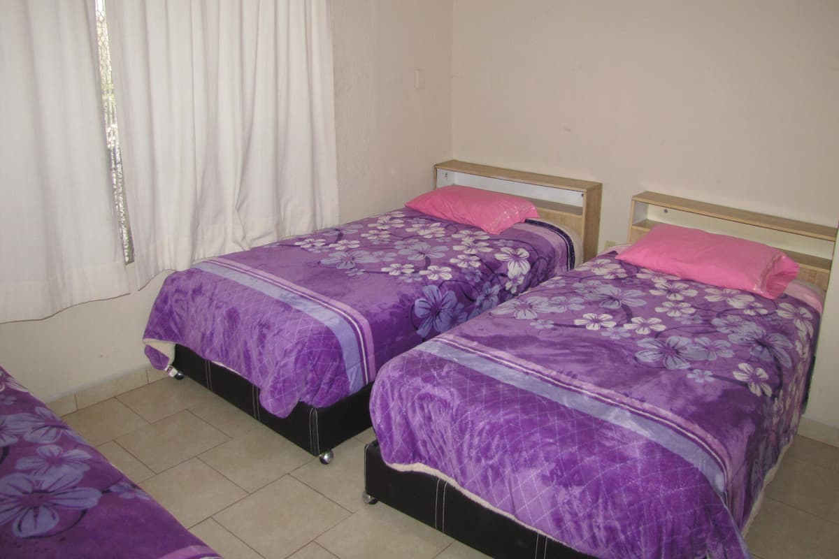Une chambre avec deux lits simples, chacun recouvert d’une couvre-lit à motifs floraux violets et doté d’une tête de lit en bois.