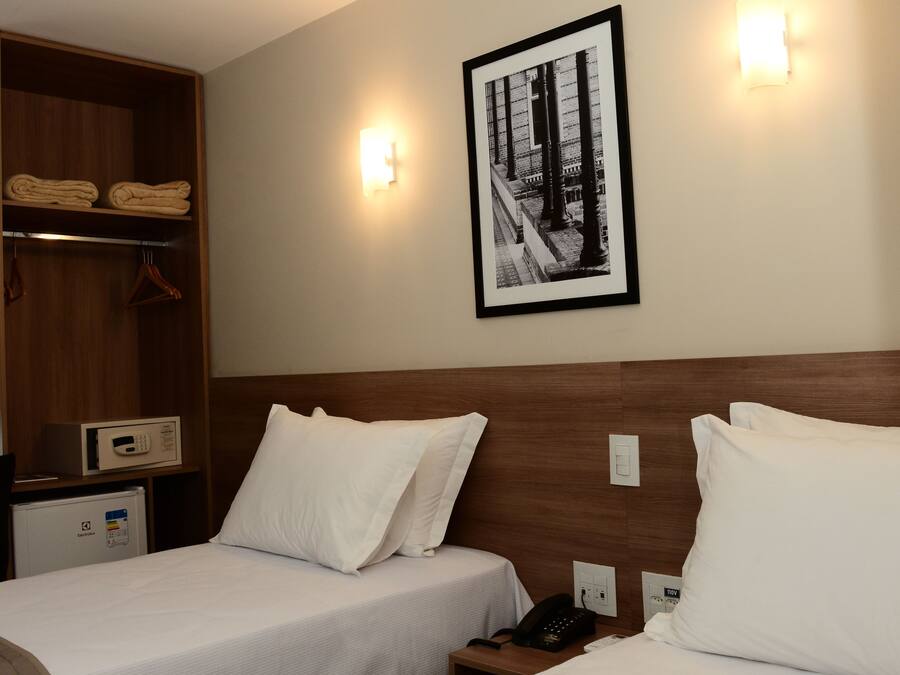 Quarto de hotel com duas camas, um guarda-roupa, uma mesa de cabeceira com telefone e um quadro na parede.