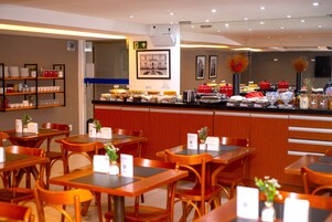 A restaurant with wooden tables and chairs, a buffet counter with various food items, and a wall-mounted menu board.