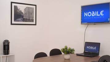 Una sala de conferències amb una taula rodona, cadires, una fotografia amb marc a la paret, un portàtil que mostra 'NOBLE HOTELS & RESORTS' i un altaveu a l'estant.