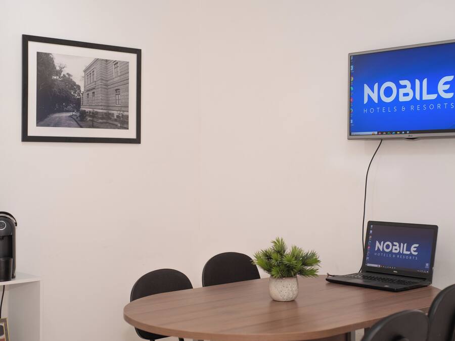Una sala de conferències amb una taula rodona, cadires, una fotografia amb marc a la paret, un portàtil que mostra 'NOBLE HOTELS & RESORTS' i un altaveu a l'estant.