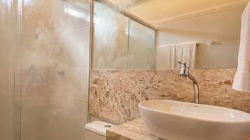 A modern bathroom with a glass shower enclosure, a toilet, a sink with a marble countertop, and a mirror.