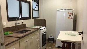 Une cuisine compacte équipée d’un évier, d’une cuisinière et d’un réfrigérateur. Un petit coin repas avec un tabouret est également prévu.