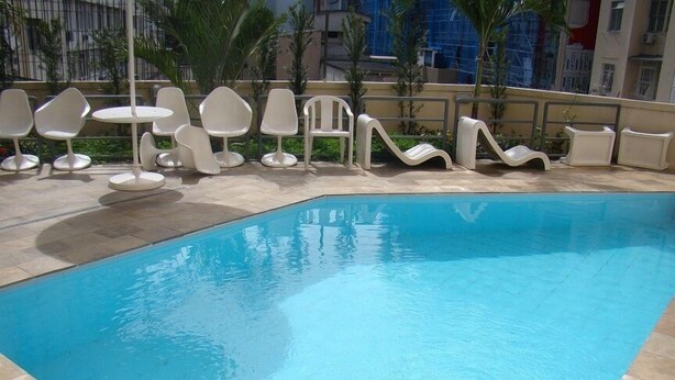 Une piscine entourée d’une terrasse carrelée et de palmiers, avec des chaises et des tables blanches.