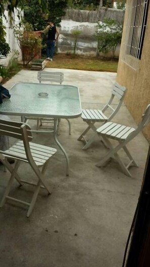 A patio with a glass-top table and four white metal chairs.