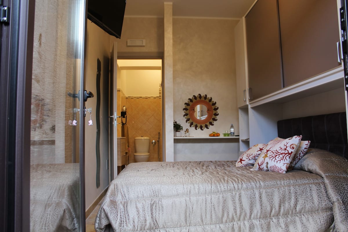 A bedroom with a bed, a shower, a toilet, and a mirror.