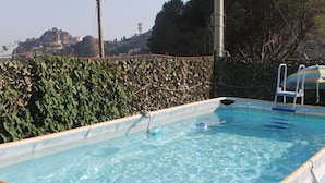 A rectangular swimming pool with clear blue water, surrounded by a hedge and a tiled roof structure. - Venere B&B Castelmola (Castelmola)