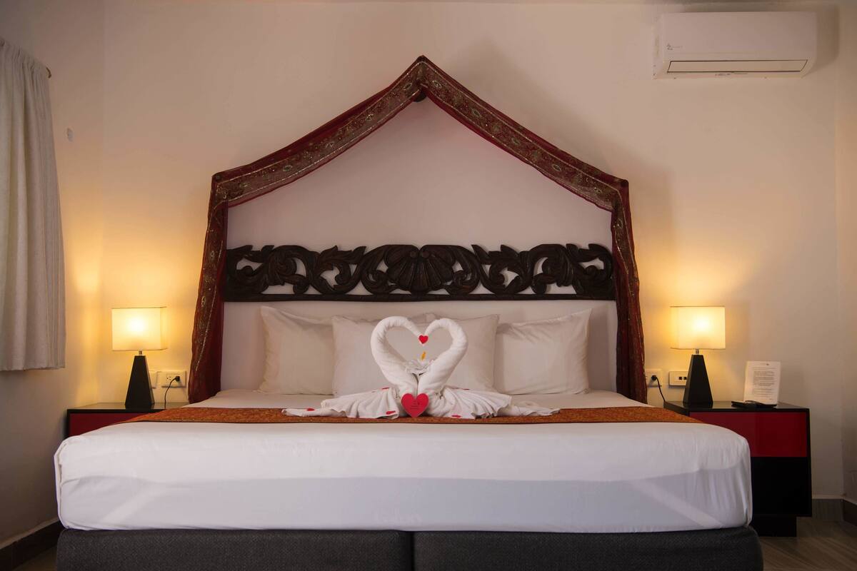 Una habitación de hotel con una cama con dosel, dos lámparas de noche y una decoración de toallas con forma de cisne.
