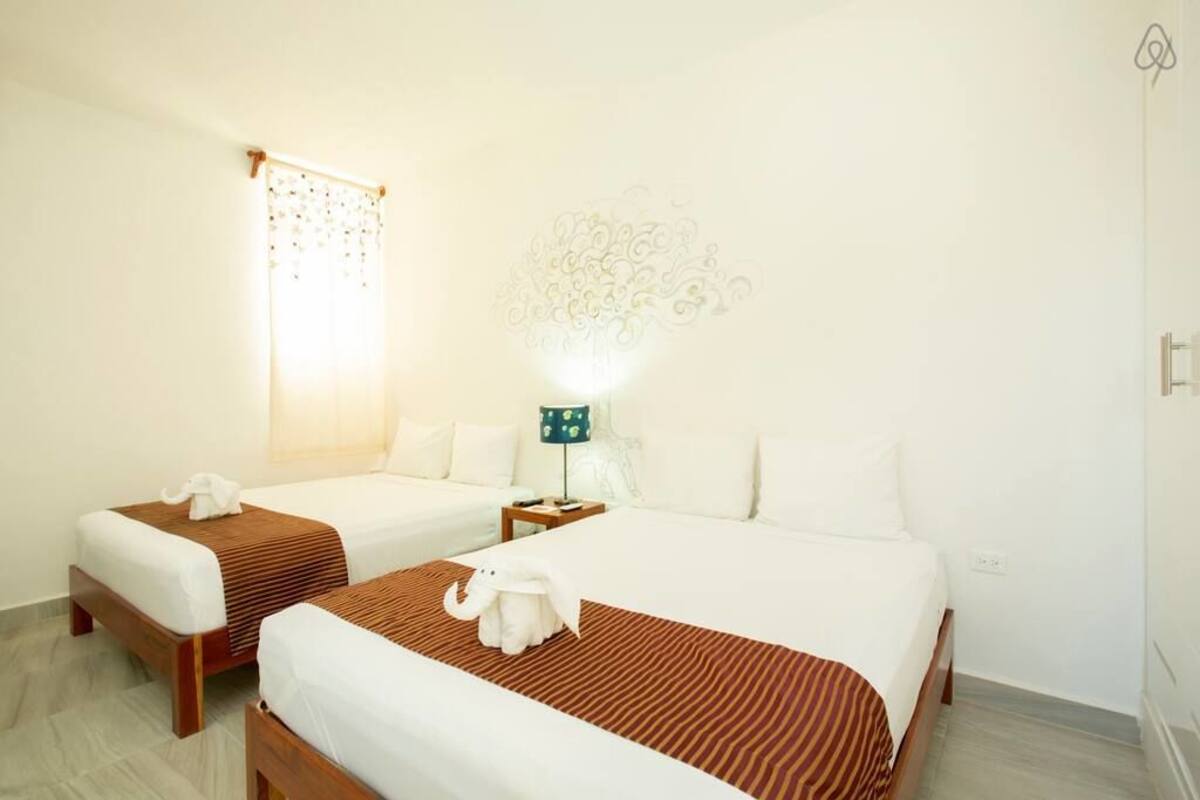 Habitación de hotel con dos camas, una mesita de noche, una lámpara y un adorno en la pared.