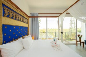 Une chambre spacieuse avec un grand lit, une tête de lit décorative, un balcon avec vue et une petite table sur laquelle est posé un vase de fleurs.