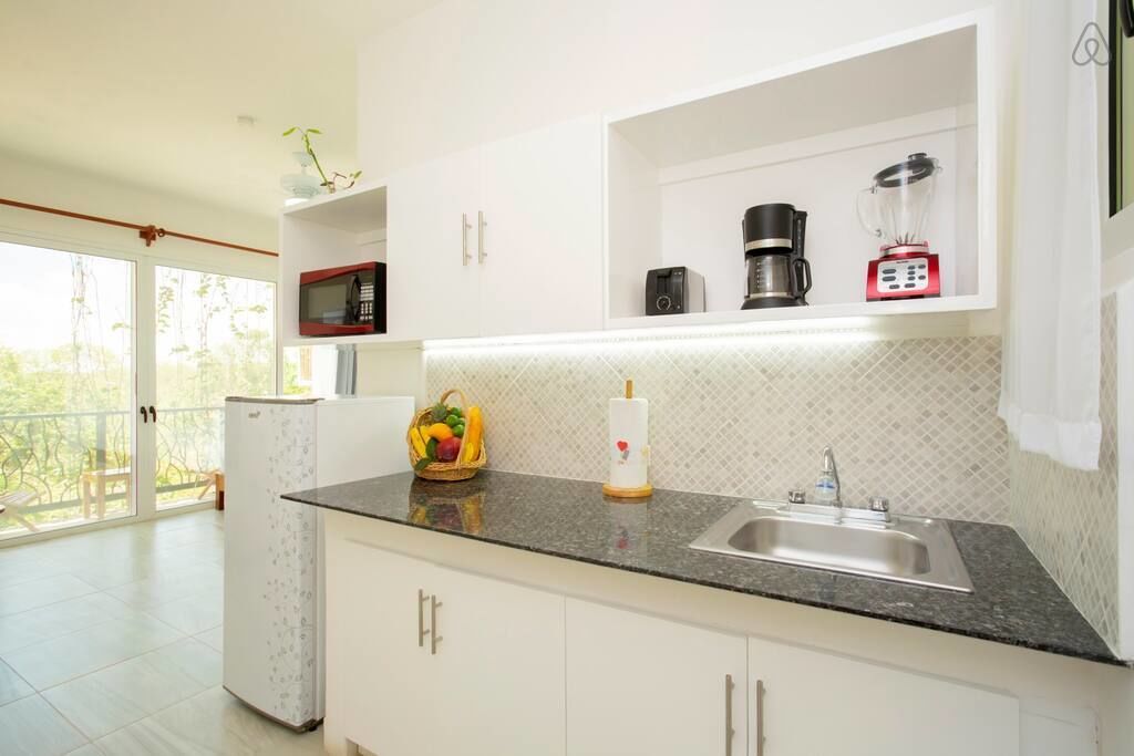 Eine moderne Küche mit weißen Schränken, einer Granit-Arbeitsplatte, einer eingebauten Mikrowelle, einer Kaffeemaschine und einem Mixer.