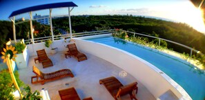 Un espace aménagé au bord de la piscine, avec des chaises longues et un coin salon abrité, offrant une vue sur un paysage luxuriant.