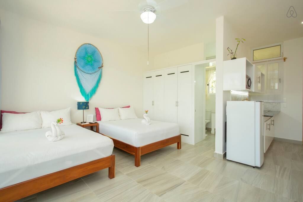 A hotel room with two beds, a wardrobe, a kitchenette, and a ceiling fan.