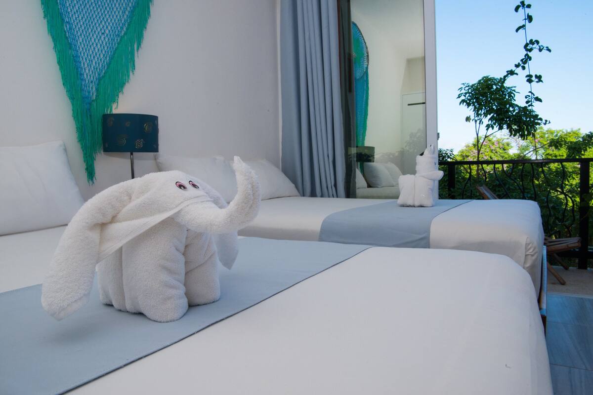 Habitación de hotel con dos camas, un balcón y vistas a árboles.
