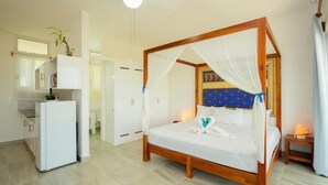 A bedroom with a four-poster bed, a small bedside table, a nightstand, a ceiling fan, and a refrigerator. - Ocean Zen Suites on 5th Avenue - Adults Only (Playa del Carmen)