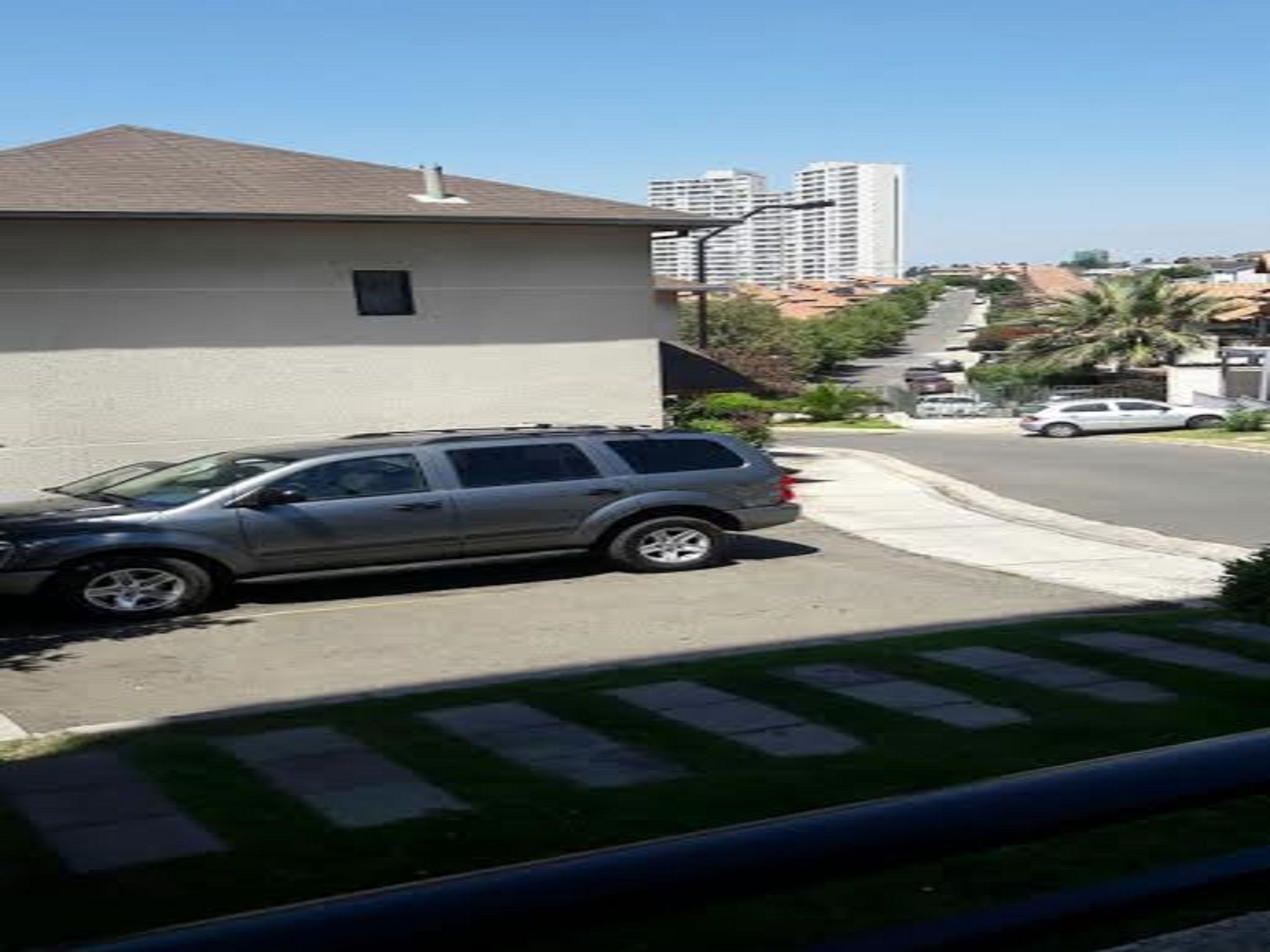 Una calle residencial con una camioneta SUV estacionada, una casa con techo inclinado y un edificio alto al fondo.