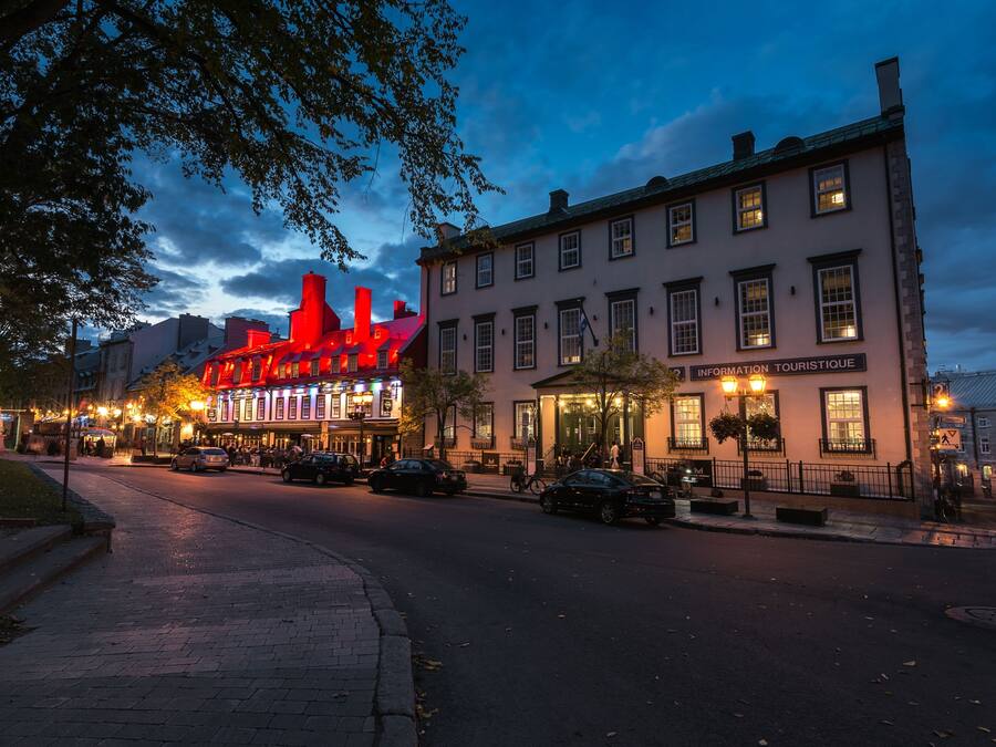 A street view at dusk with a building labeled "INFORMATION TOURISTIQUE" and a brightly lit red building in the background.