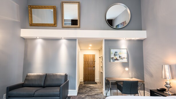 Una habitación de hotel moderna con un sofá gris, un escritorio, una cama y un espejo grande.