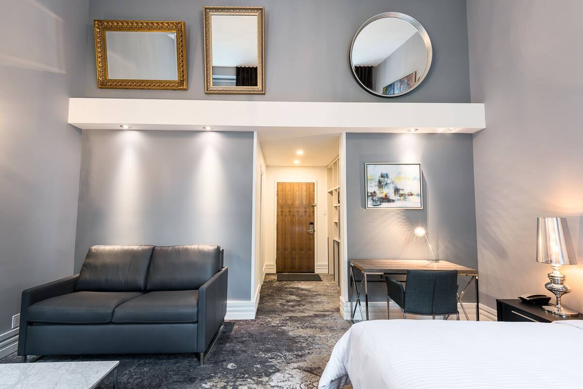 Una habitación de hotel moderna con un sofá gris, un escritorio, una cama y un espejo grande.
