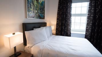 A neatly made bed with white linens, a bedside table with a lamp, and a painting on the wall.