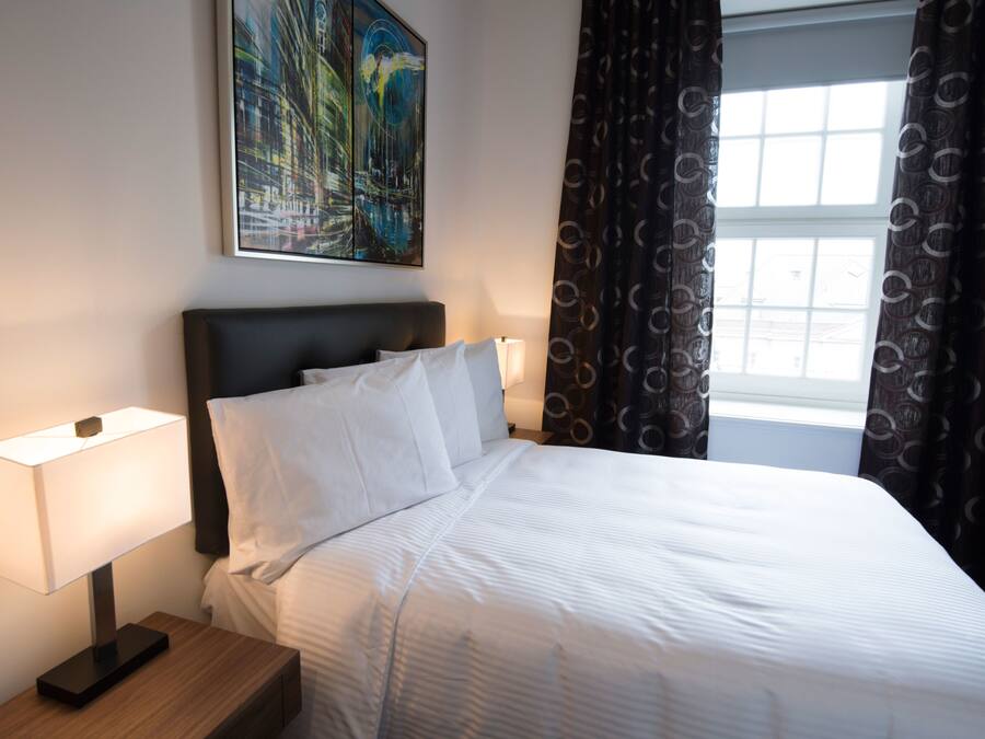 A neatly made bed with white linens, a bedside table with a lamp, and a painting on the wall.