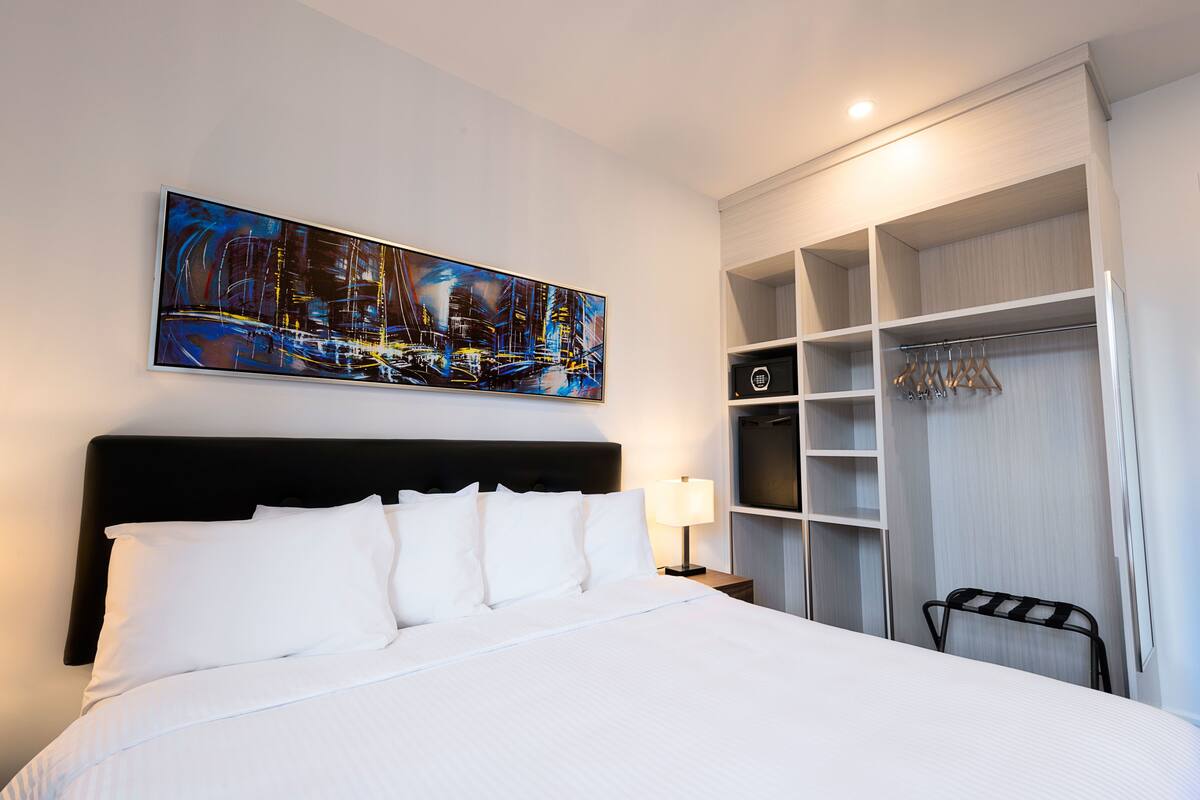 Una habitación de hotel con una cama grande, un cuadro en la pared, un vestidor y una silla.