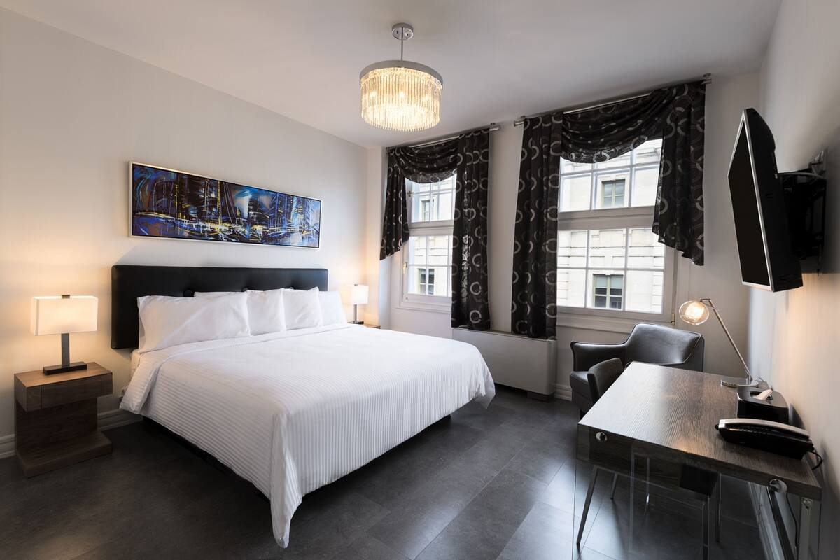 Una habitación de hotel con una cama grande, un escritorio, una silla, un televisor y un cuadro en la pared.
