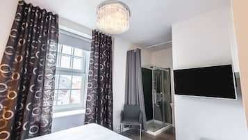 Quarto de hotel com cama, televisão, chuveiro e uma cadeira.