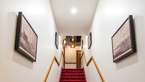 Una escalera con alfombra roja que conduce a una habitación con piso de madera y pared blanca.