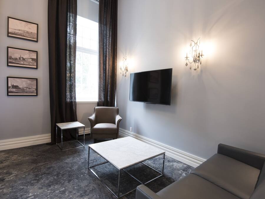 Ein modernes Hotelzimmer mit großem Fenster, einem wandmontierten Flachbildfernseher, einer Couch, einem Sessel, einem kleinen Tisch und drei gerahmten Bildern an der Wand.