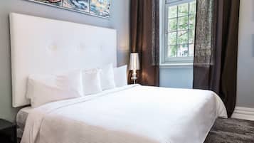 A bedroom with a large bed, a headboard, a window with curtains, and a painting on the wall.