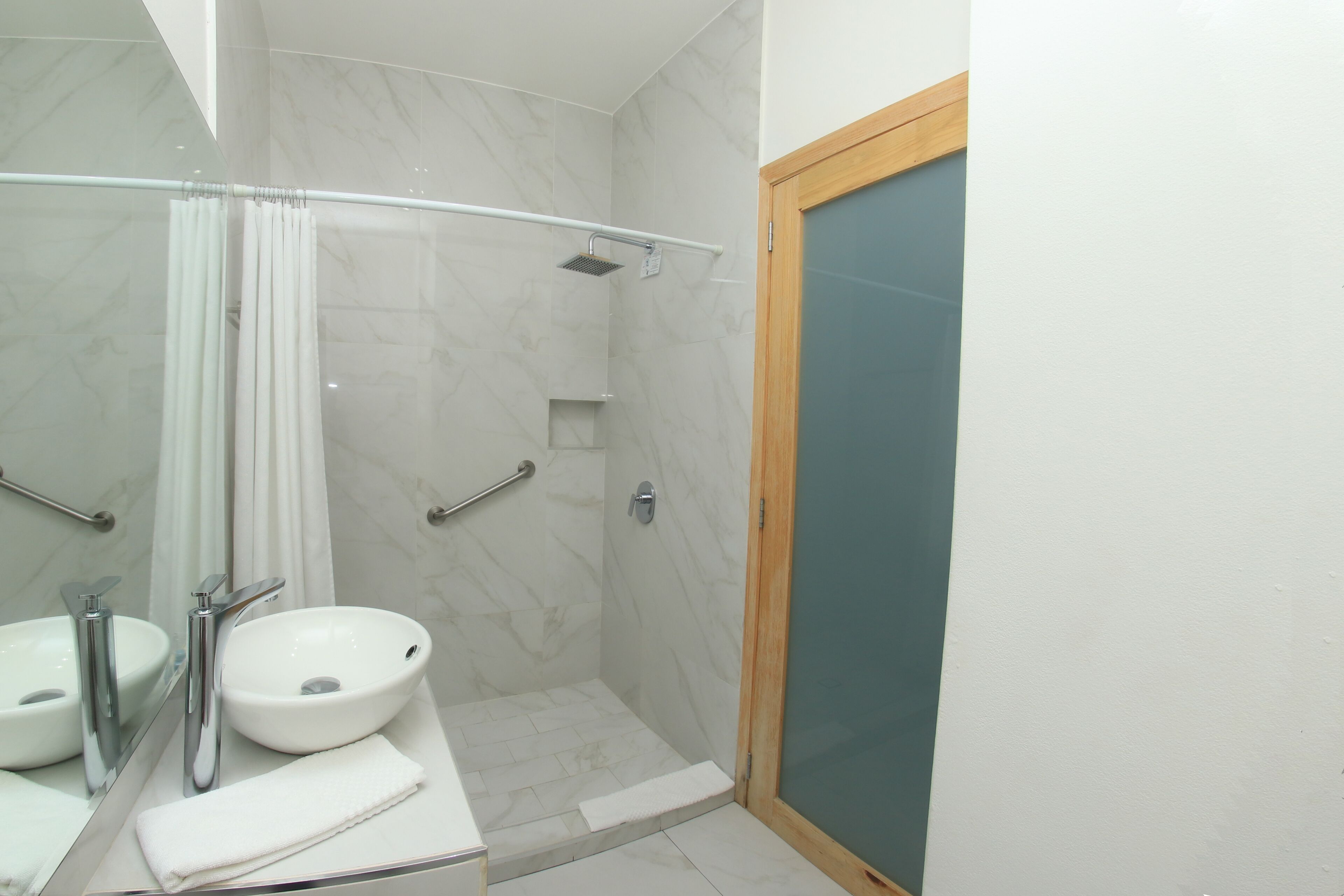 Un baño con lavamanos, espejo y ducha blancos.