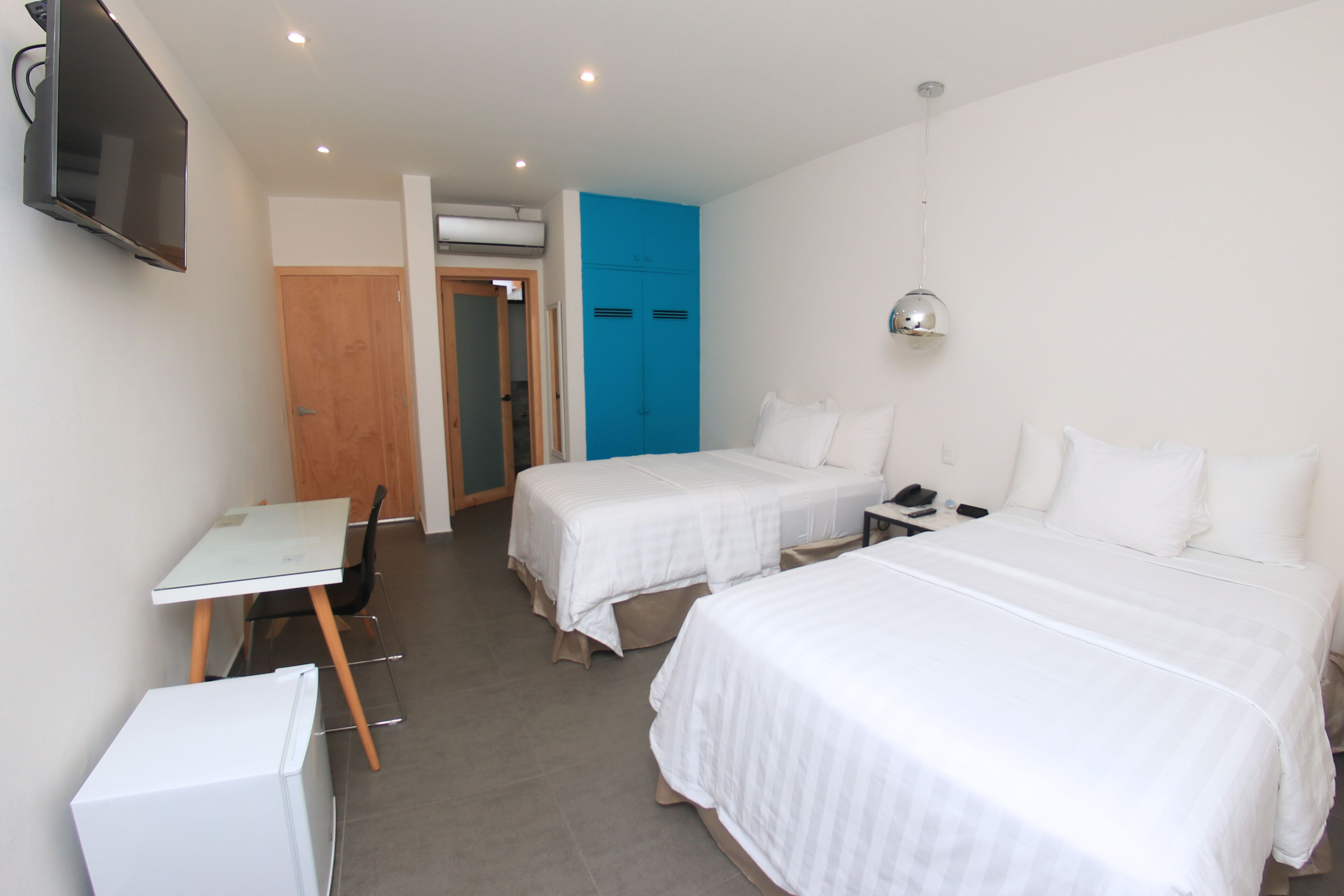 A hotel room with two beds, a desk, a chair, a TV, and a wardrobe.