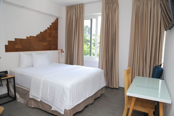 Habitación de hotel con cama, escritorio y ventana con cortinas.