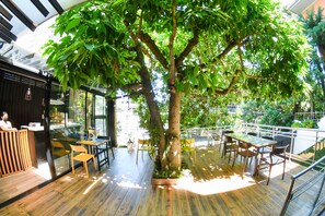 An indoor area with a wooden floor, a large tree, and several tables and chairs. - Kaleo Hotel Boutique (San Salvador)