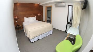 Moderni hotellihuone, jossa on sänky, vihreä tuoli, pieni pöytä ja peili.