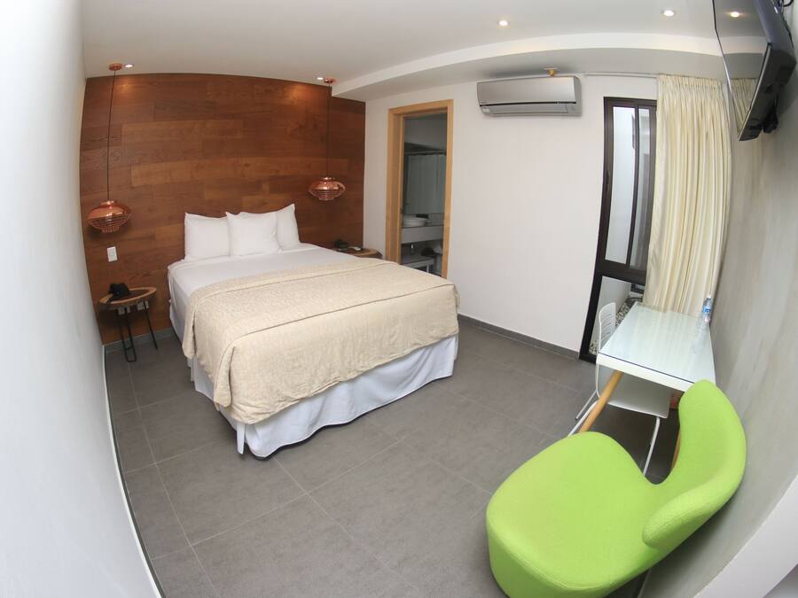A modern hotel room with a bed, a green chair, a small table, and a mirror.