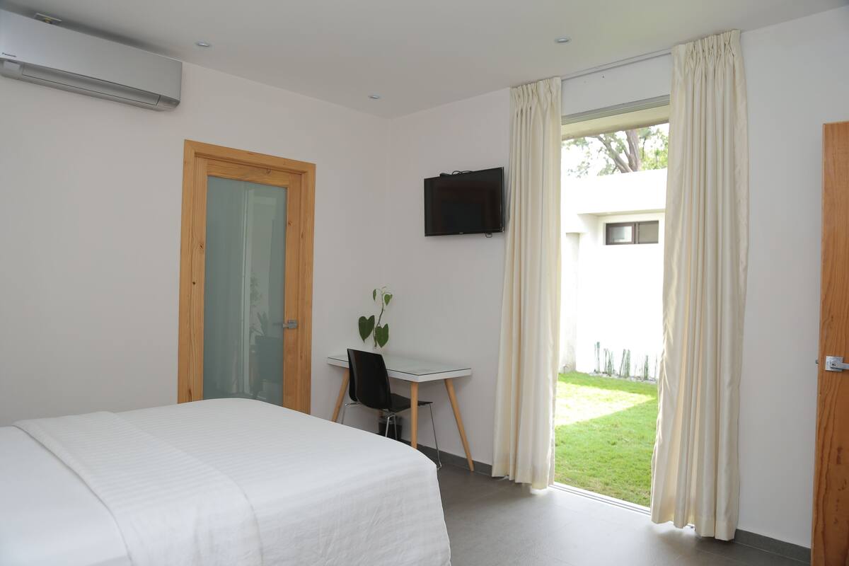 A bedroom with a bed, a desk with a chair, a television, and a window with curtains.