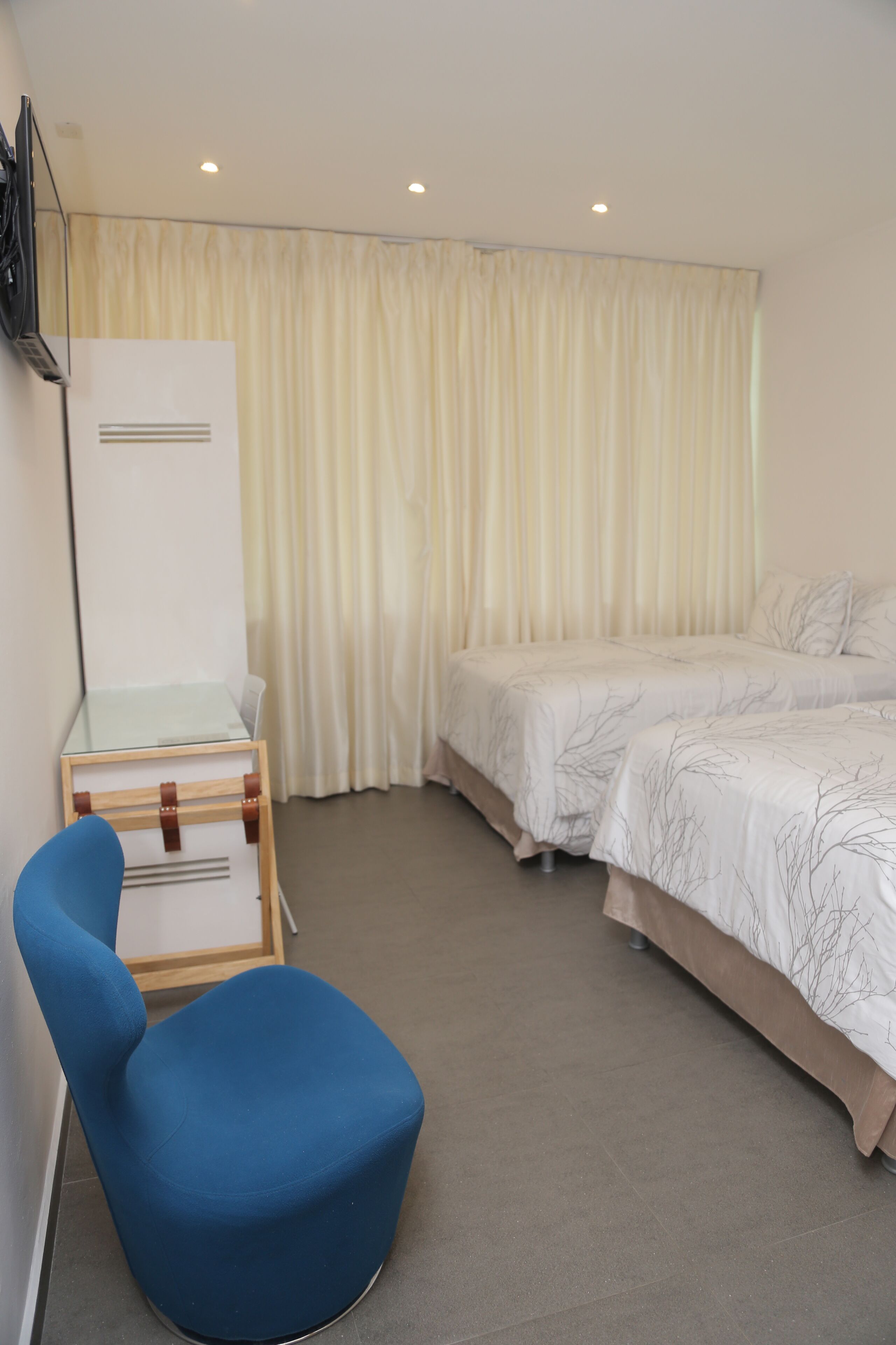 Habitació d'hotel amb un llit individual, una taula amb cadira i una finestra gran amb cortines.