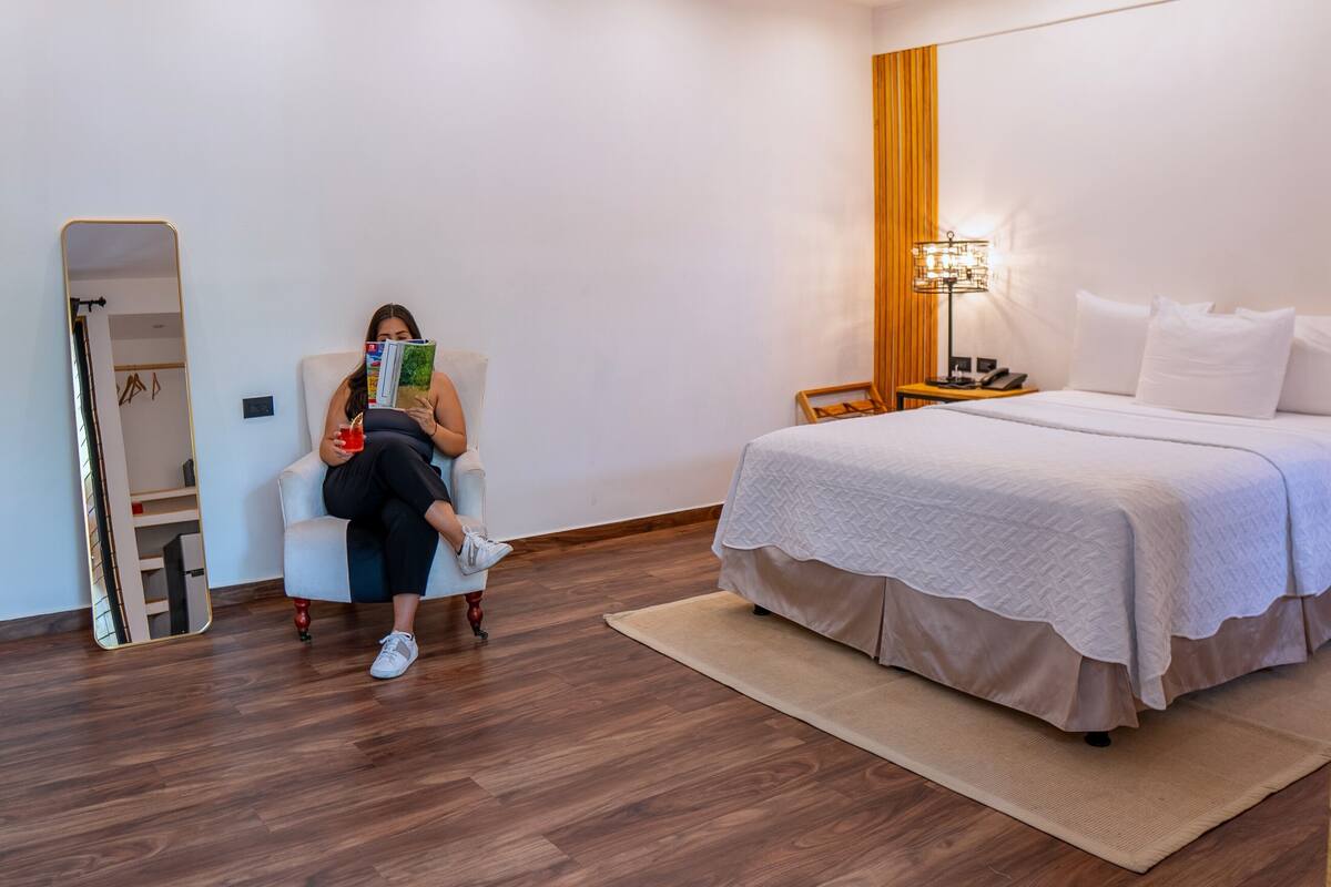 A hotel room with a bed, a bedside table with a lamp, a mirror, and a chair.