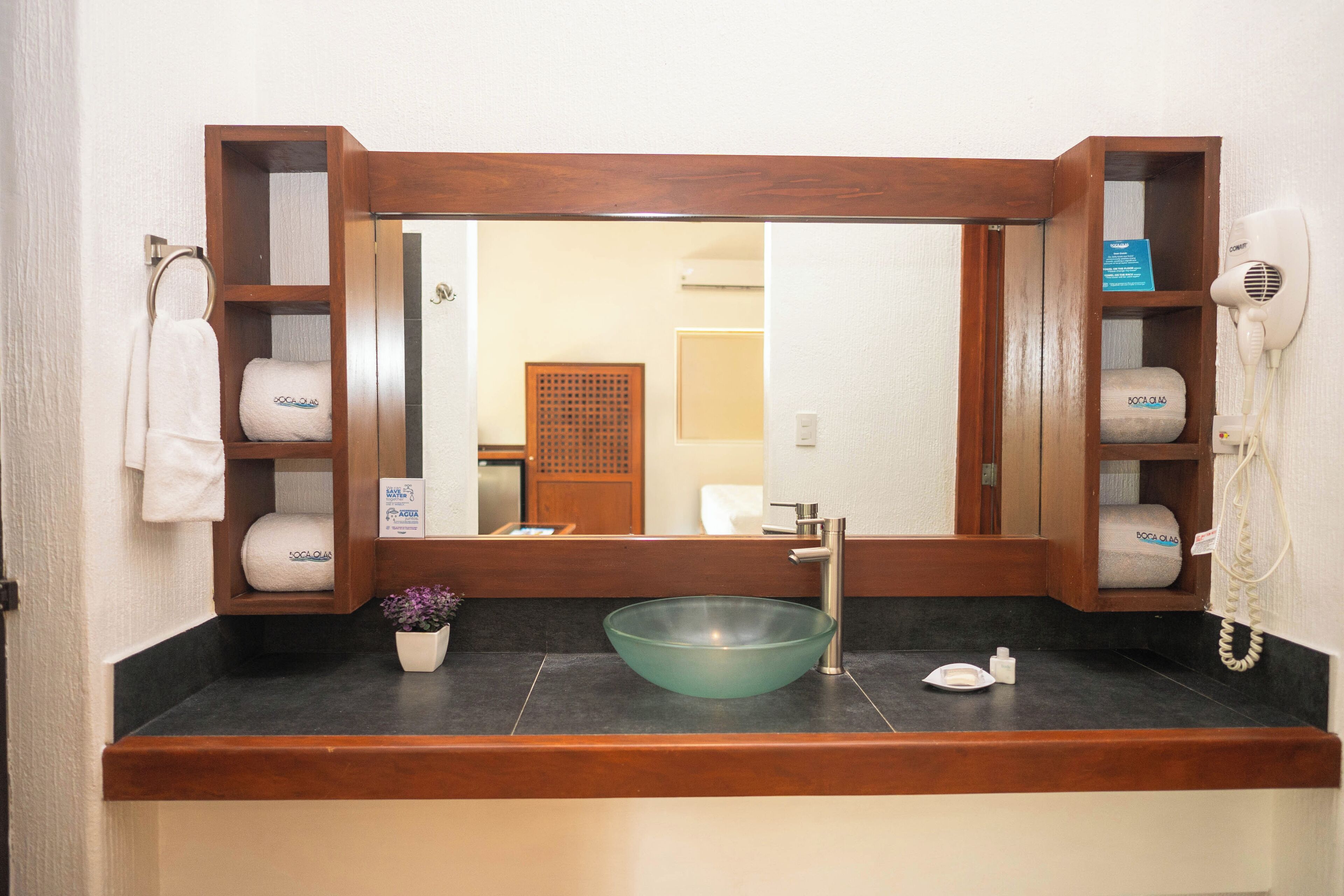 Un baño con tocador de madera, lavamanos de vidrio, toallero y secador de pelo.