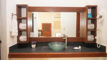 Un baño con tocador de madera, lavamanos de vidrio, toallero y secador de pelo.