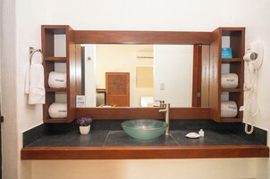 Un baño con tocador de madera, lavamanos de vidrio, toallero y secador de pelo.