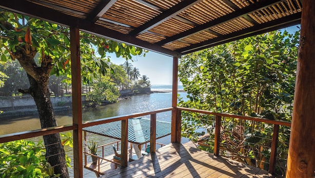 A wooden deck with a view of a calm body of water and lush greenery. - Boca Olas Resort Villas (Tamanique)