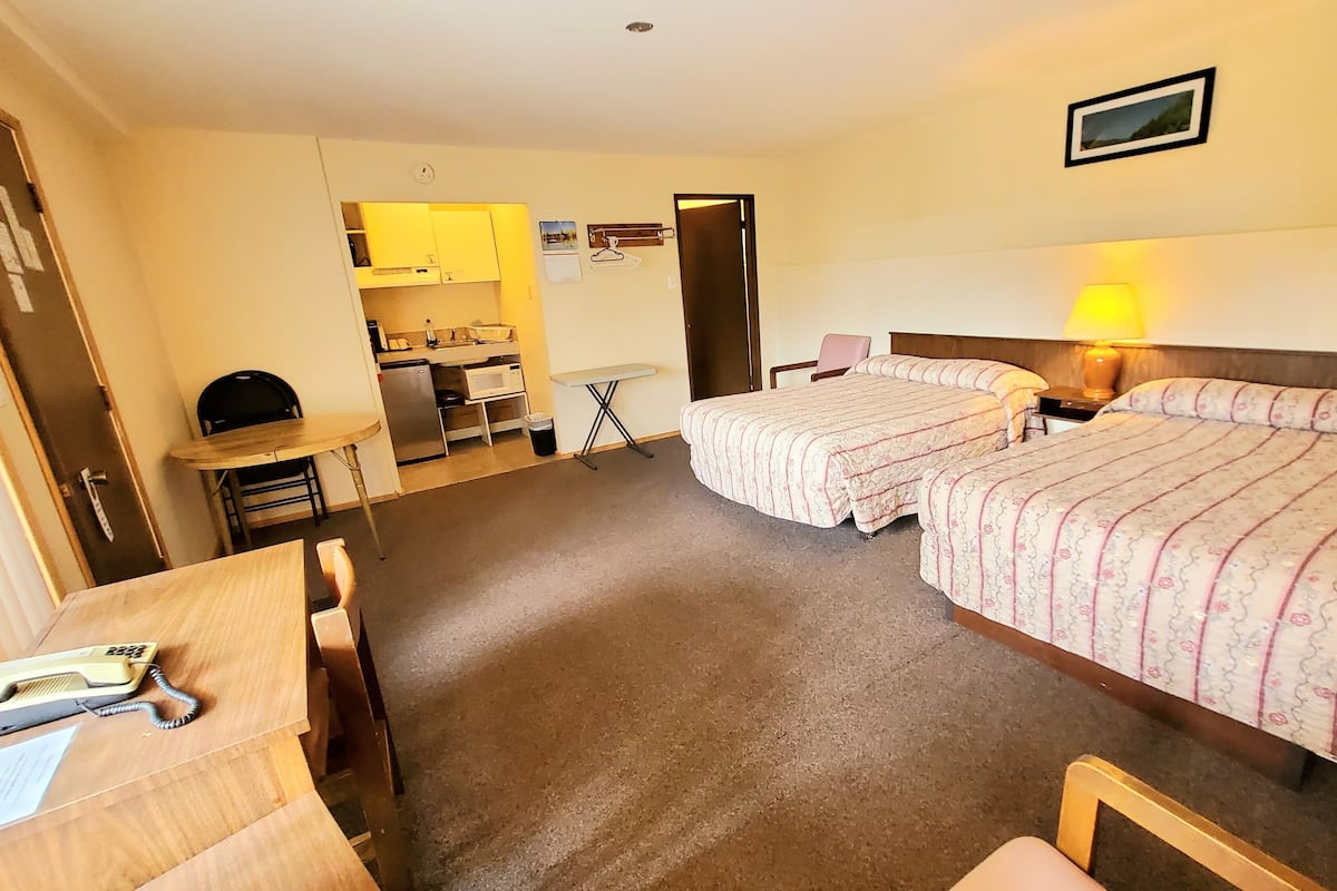 A hotel room with two beds, a desk, a chair, a small kitchenette, and a bathroom.