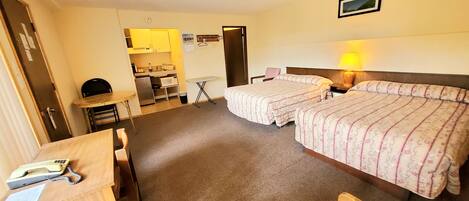 Une chambre d’hôtel avec deux lits, un bureau, une chaise, une petite kitchenette et une salle de bain.