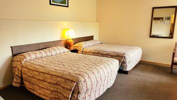 Ein Hotelzimmer mit zwei Betten, einem Nachttisch mit Lampe, einem Sessel und einem Spiegel an der Wand.